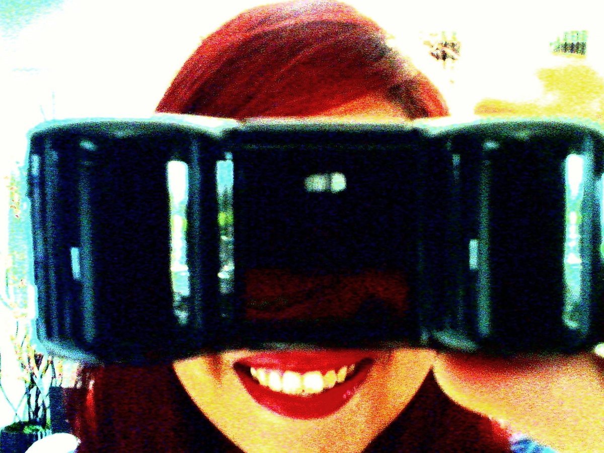 Alissa grinning behind a chunky toy camera, shot with a Digital Harinezumi